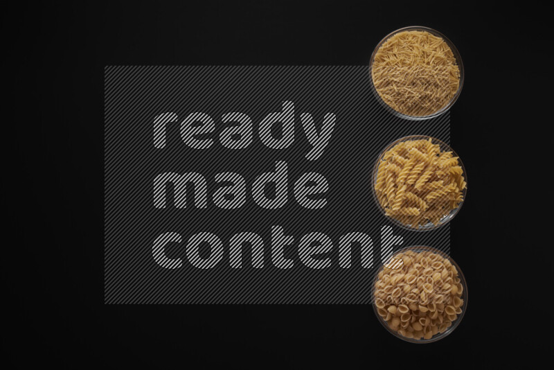 Different pasta types in 3 glass bowls on black background