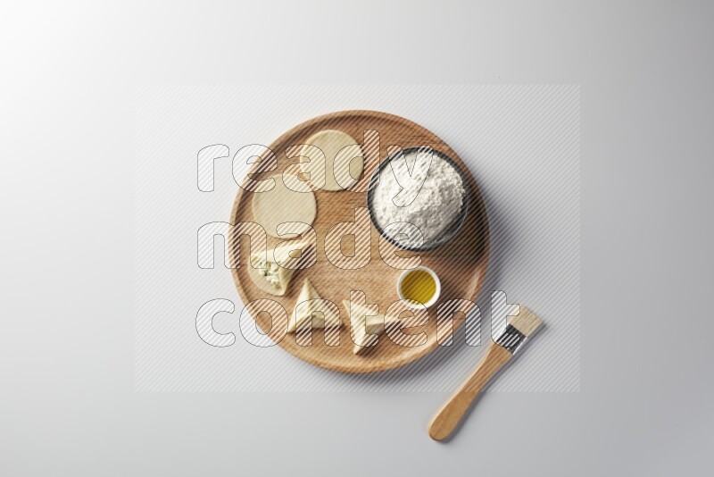 two closed sambosas and one open sambosa filled with cheese while flour, and oil with oil brush aside in a wooden dish on a white background