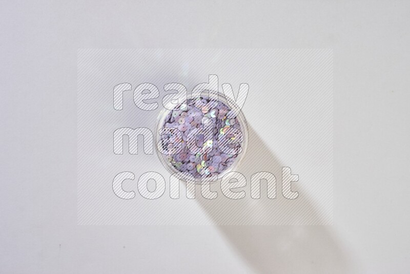 Colored flat sequins in a glass jar on grey background