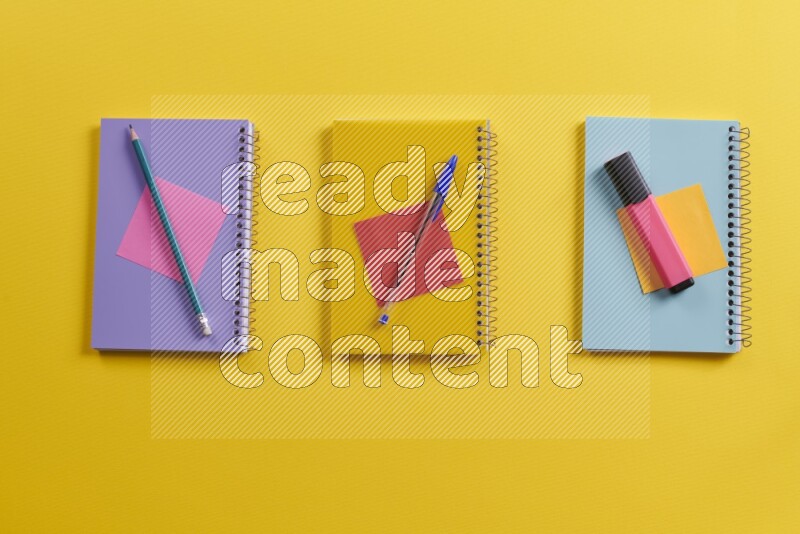 Multicolored notebooks with school supplies on yellow background
