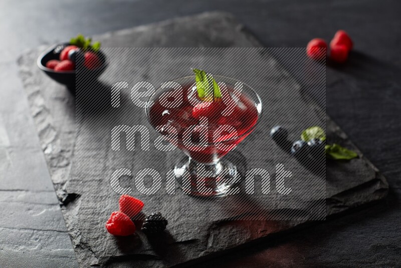 A glass of mixed berries juice with mint leaves on black background