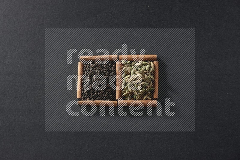 مربعان من أعواد القرفة ممتلئان بحبوب الفلفل الأسود وحب الهيل علي خلفية سوداء