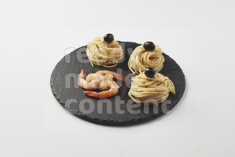 spaghetti nests with white sauce and shrimp on a black slate on a white background