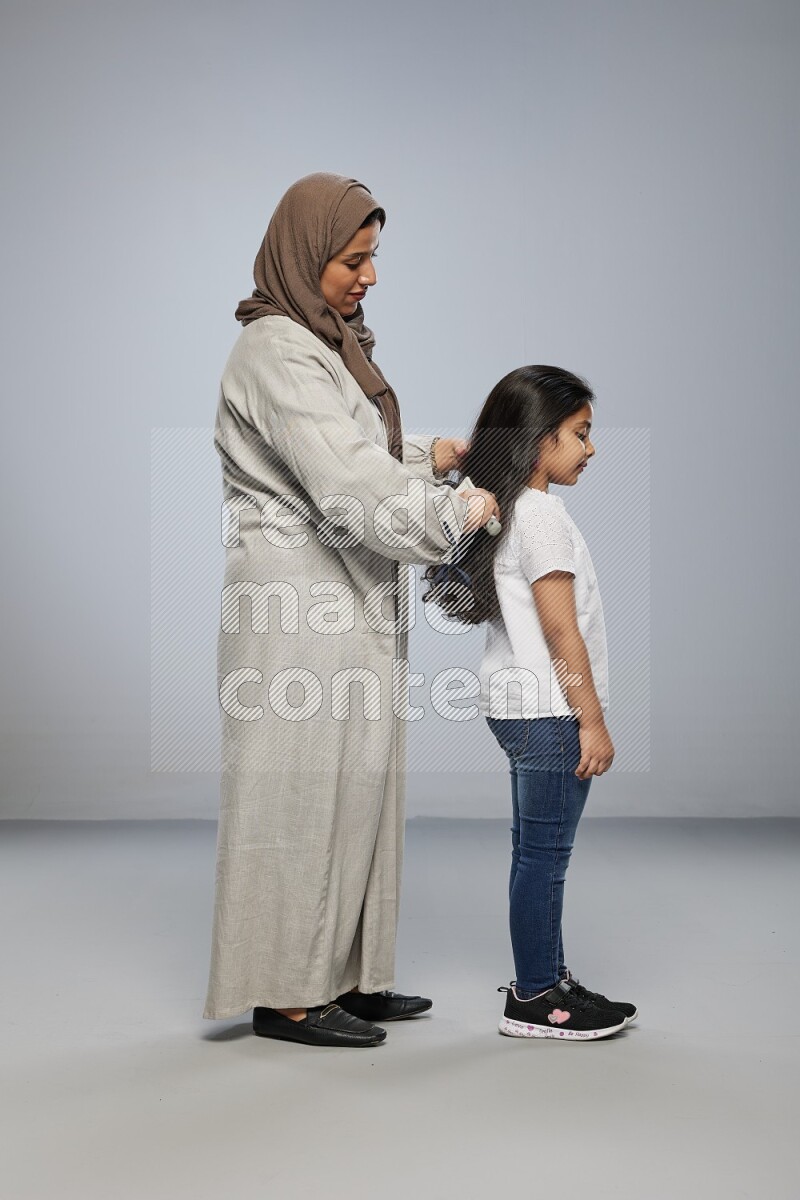 Mom standing styling hair for her daughter on gray background