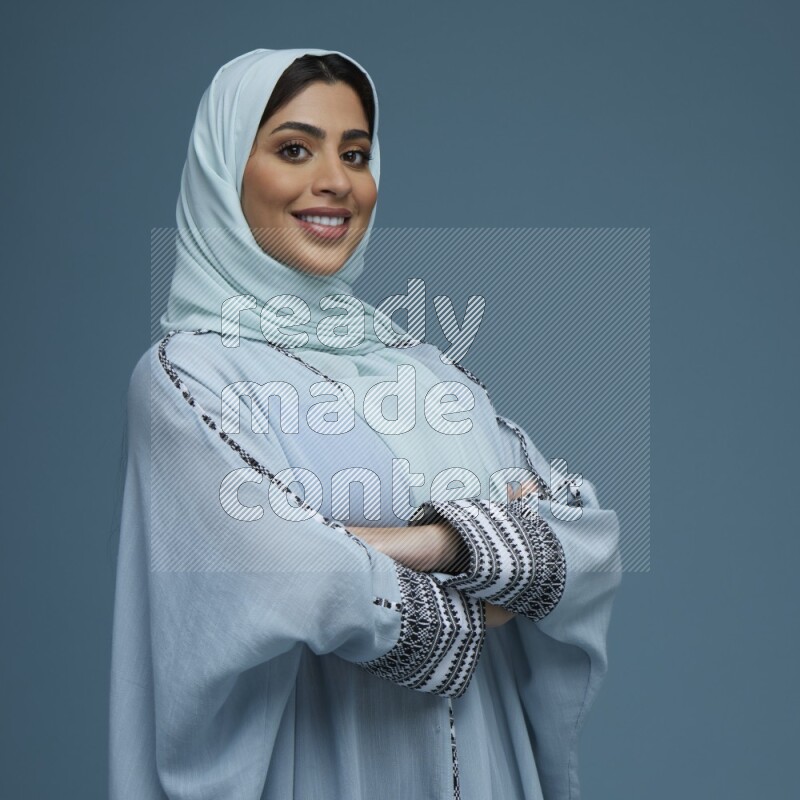 A woman posing in a blue background wearing a blue Abaya with hijab