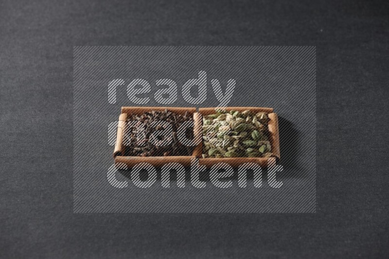 مربعان من أعواد القرفة ممتلئان بحبوب الهيل والقرنفل علي خلفية سوداء