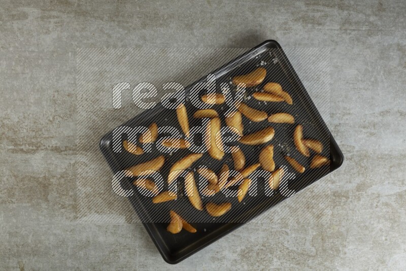 wedges potato in a black stainless steel rectangle tray on grey textured counter top