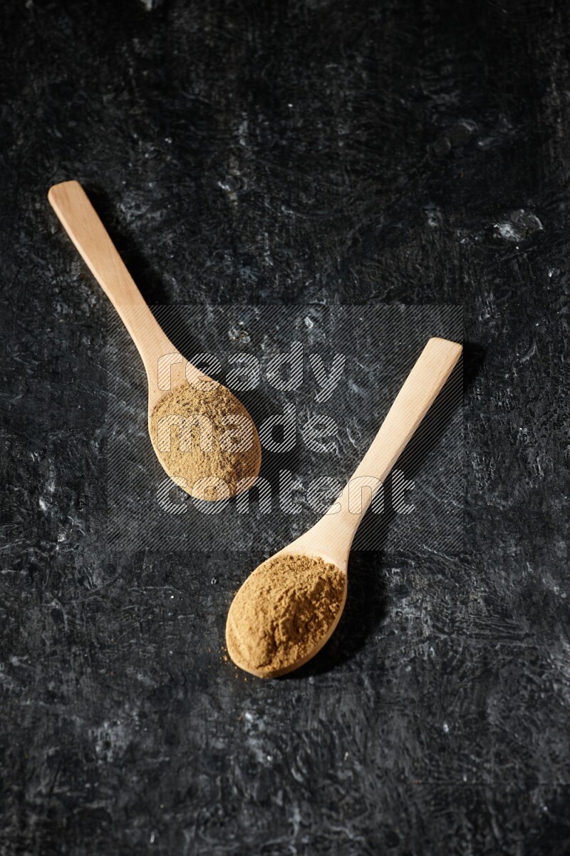 Wooden spoons full of allspice powder on a textured black flooring