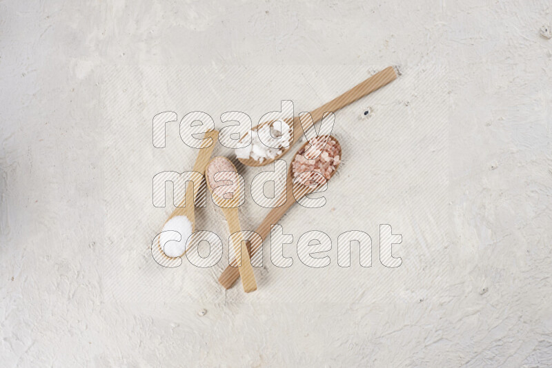 4 wooden spoons filled with fine and coarse salt on white background