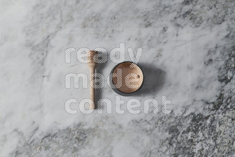 Multicolored pottery bowl with wooden honey dipper on the side on grey marble background