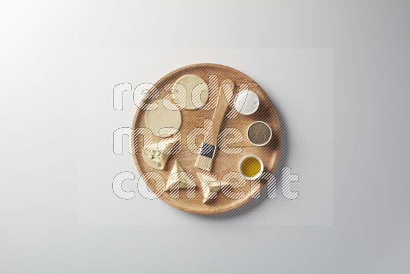 two closed sambosas and one open sambosa filled with cheese while salt, black pepper and oil with oil brush aside in a wooden dish on a white background