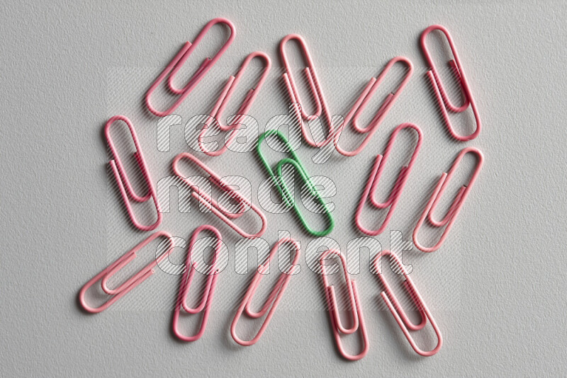 A bunch of pink paper clips with a different colored paper clip in the center on grey background