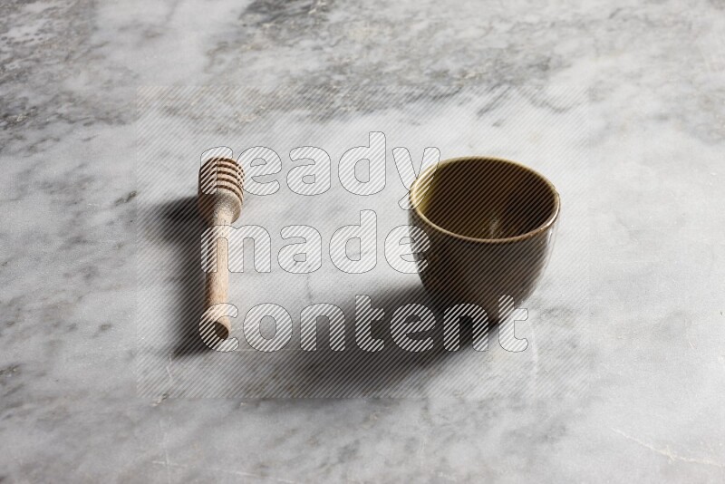 Multicolored pottery cup with wooden honey dipper on the side on grey marble background