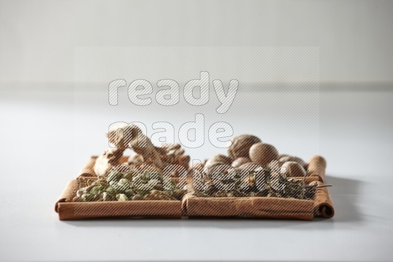 4 مربعات من أعواد القرفة ممتلئة بجوزة الطيب والزنجبيل المجفف والهيل والريحان المجفف على أرضية بيضاء