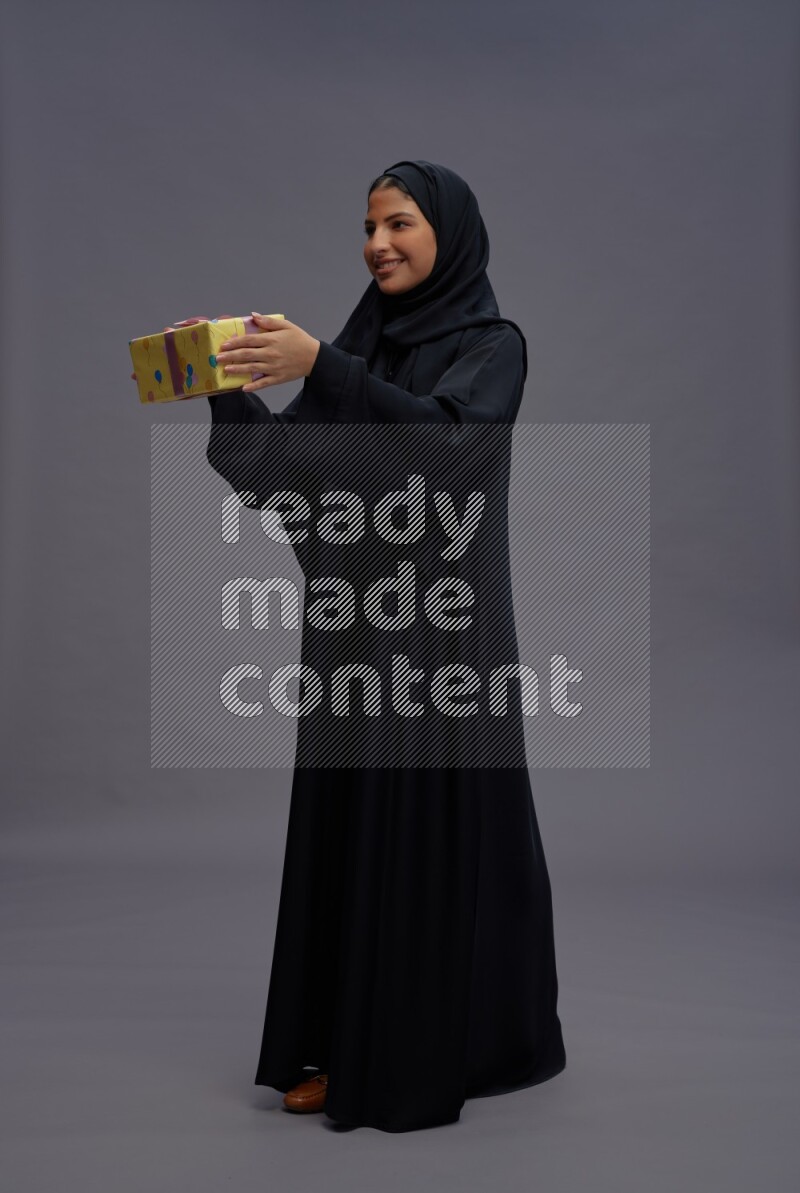 Saudi woman wearing Abaya standing holding gift box on gray background