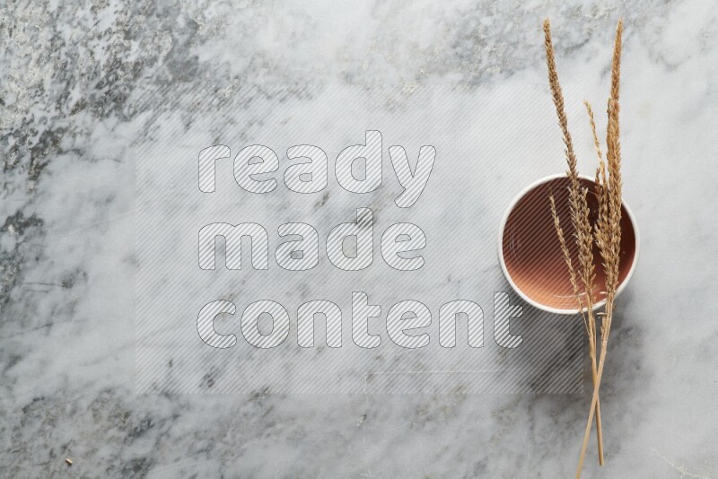 Wheat stalks on brown pottery bowl on grey marble background