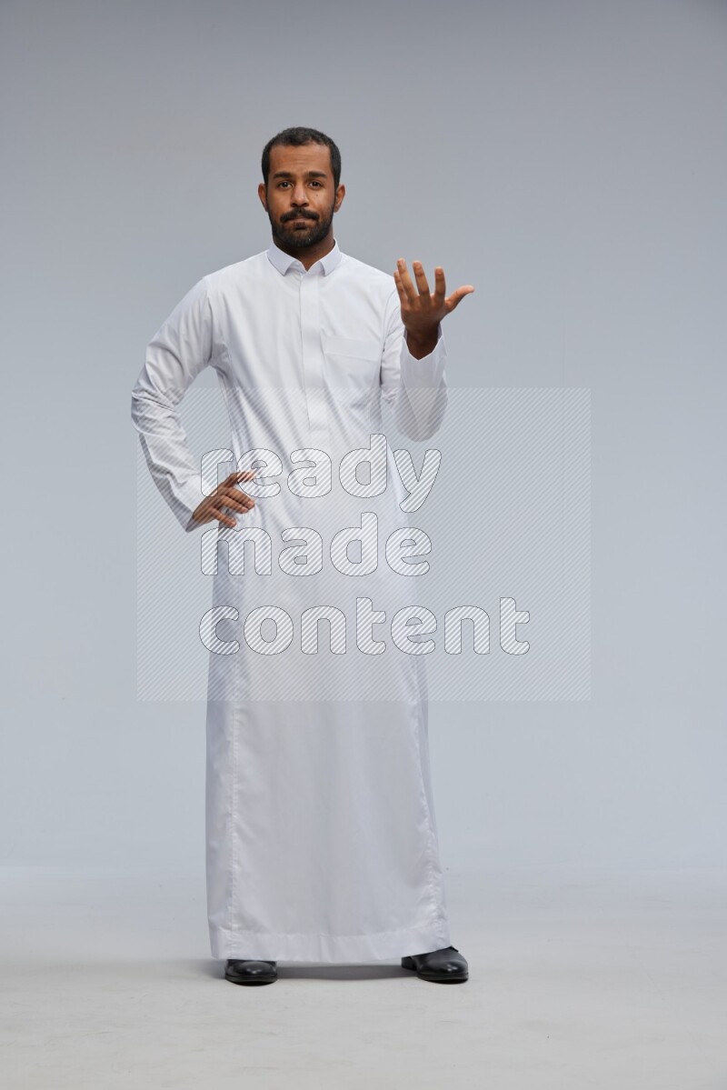 Saudi man Wearing Thob standing interacting with the camera on Gray background