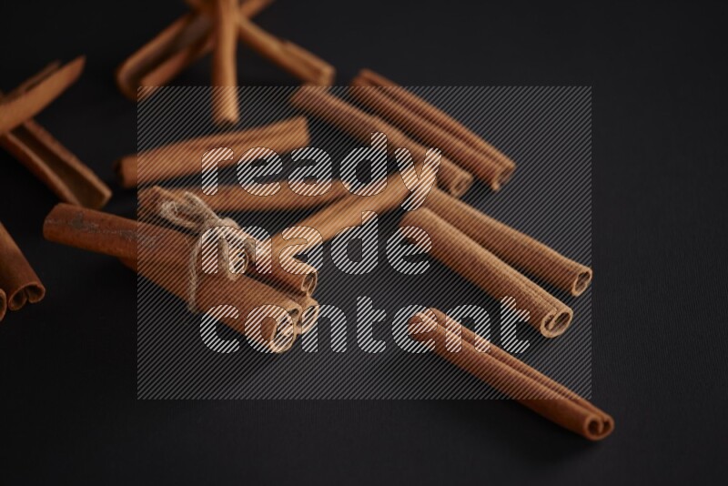 4 Cinnamon sticks stacked and bounded with more sticks in the background on black flooring