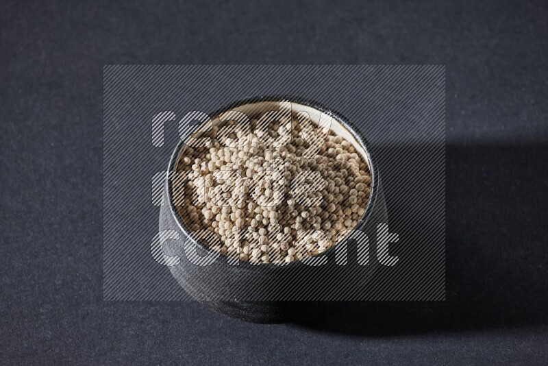 Black pottery bowl full of white pepper on black flooring