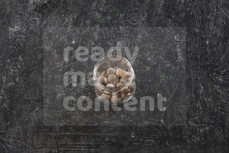 A glass jar full of whole nutmeg seeds on a black flooring