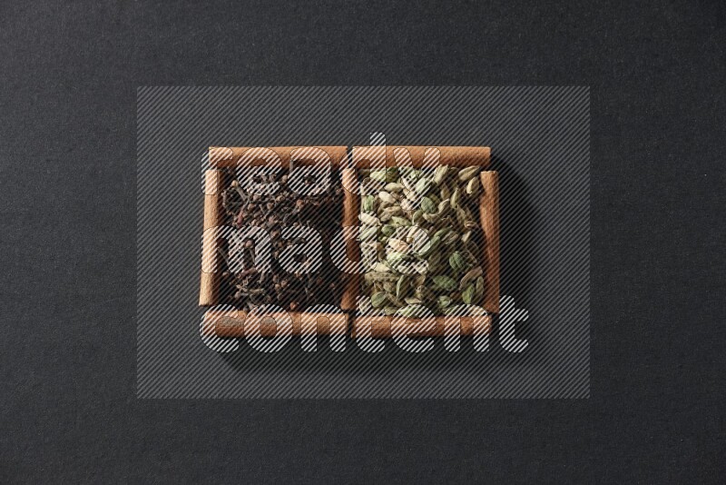 مربعان من أعواد القرفة ممتلئان بحبوب الهيل والقرنفل علي خلفية سوداء