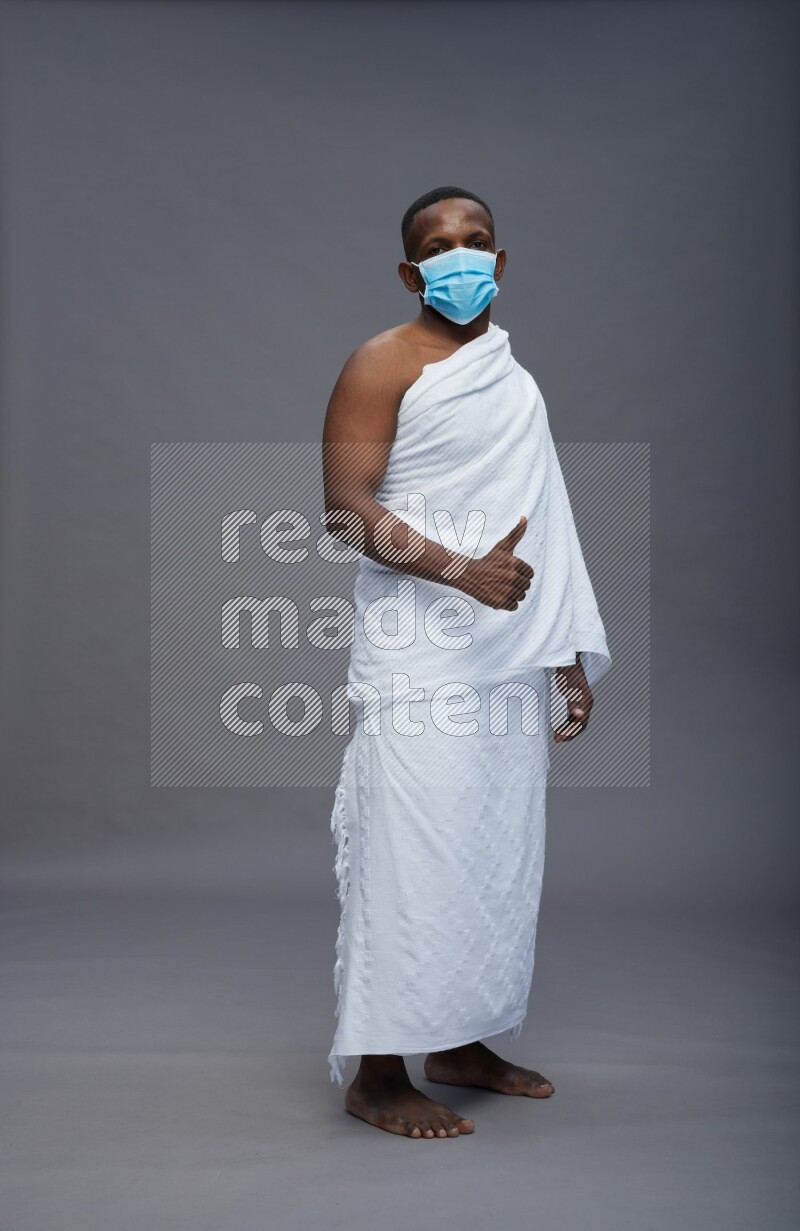 A man wearing Ehram with face mask Standing Interacting with the camera on gray background