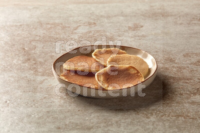 Five stacked plain mini pancakes in an irregular plate on beige background