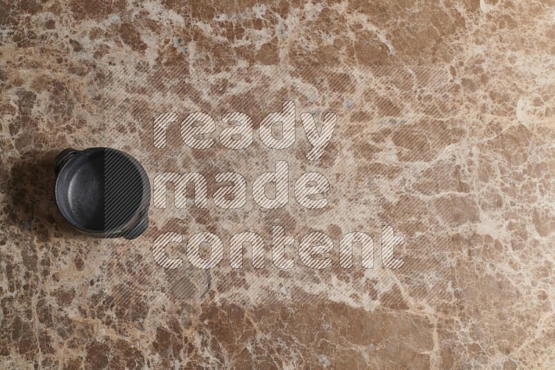 A black pottery bowl on beige marble background