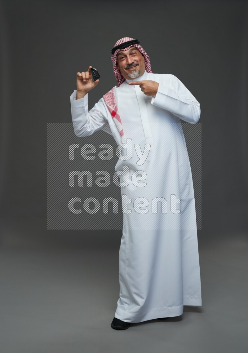 Saudi man with shomag Standing holding car key on gray background