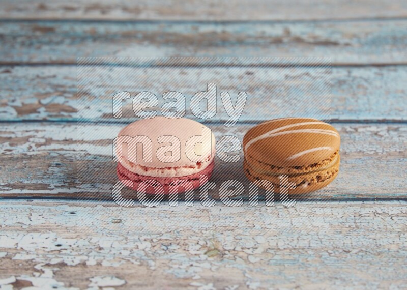 45º Shot of of two assorted Brown Irish Cream, and Pink Litchi Raspberry macarons on light blue background