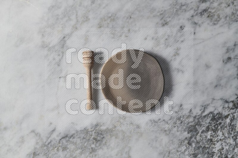 Multicolored pottery plate with wooden honey dipper on the side on grey marble background
