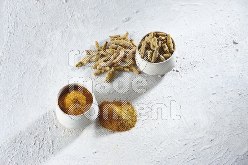 وعاءان فخاريان بيج ممتلئان ببودرة الكركم وأصابع الكركم المجففة، مع بودرة وأصابع الكركم بجانبهما على خلفية بيضاء