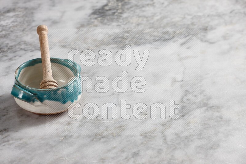 Multicolored pottery bowl with wooden honey dipper in it on grey marble background