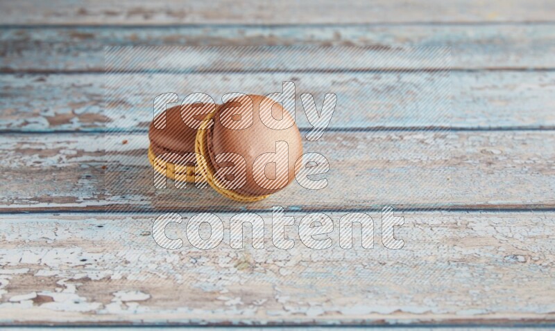 45º Shot of two Yellow and Brown Chai Latte macarons on light blue wooden background