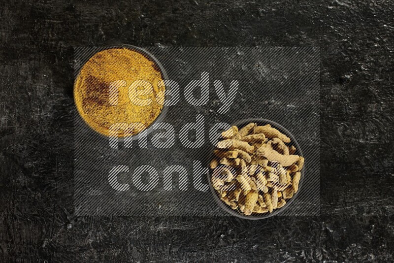 وعاءان من الفخار باللون الأسود، أحدهما ممتلئ ببودرة الكركم والآخر ممتلئ بأصابع كاملة من الكركم المجفف على خلفية سوداء