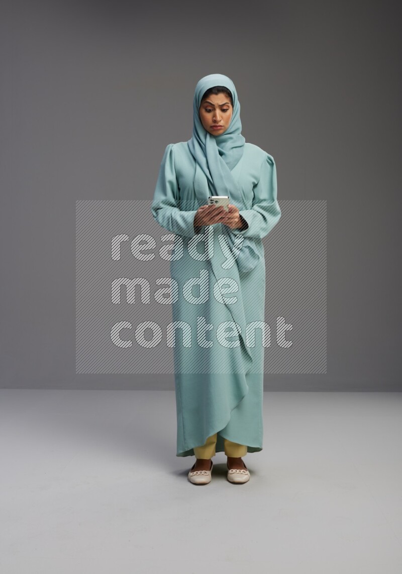 Saudi Woman wearing Abaya standing texting on phone on Gray background