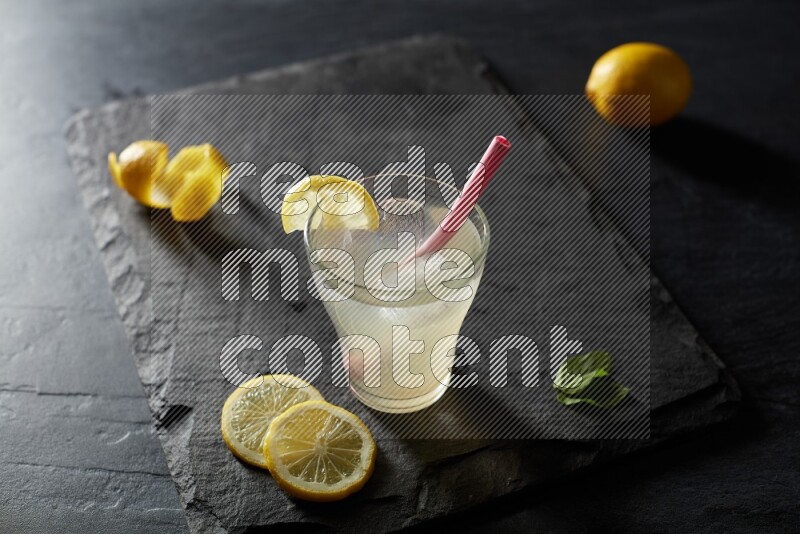 A glass of lemon juice with a straw on black background
