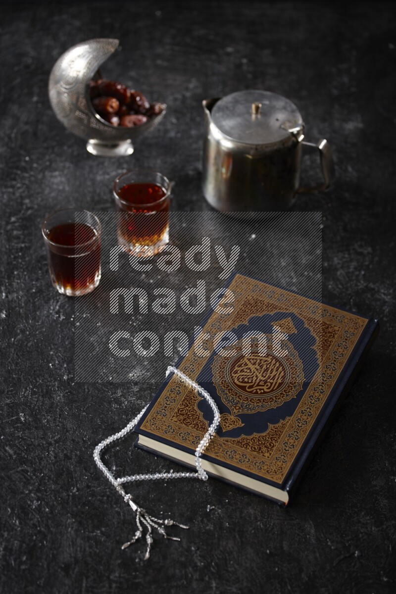 Moshaf with tea cups and prayer beads in a dark setup