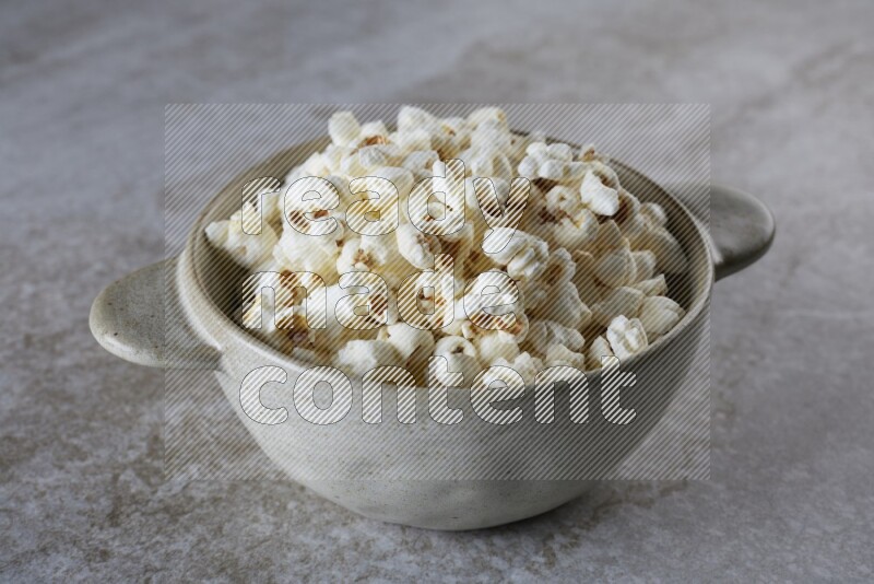 popcorn in a off-white handheld ceramic bowl on a grey textured countertop