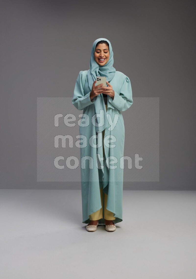 Saudi Woman wearing Abaya standing texting on phone on Gray background