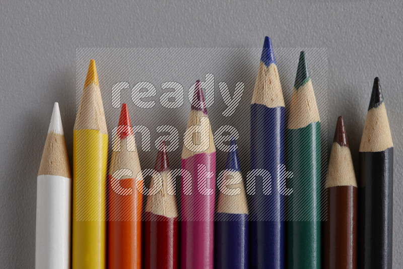 A collection of colored pencils arranged showcasing a gradient of different hues on grey background