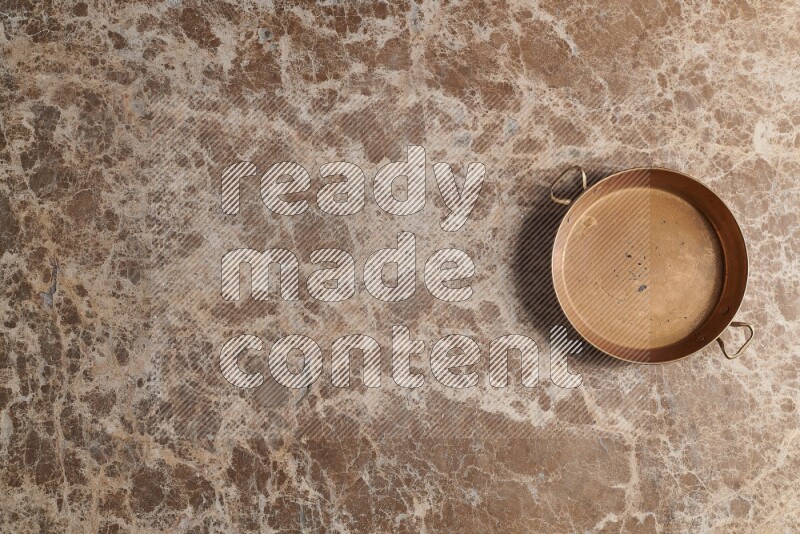 A small copper pan on beige marble background