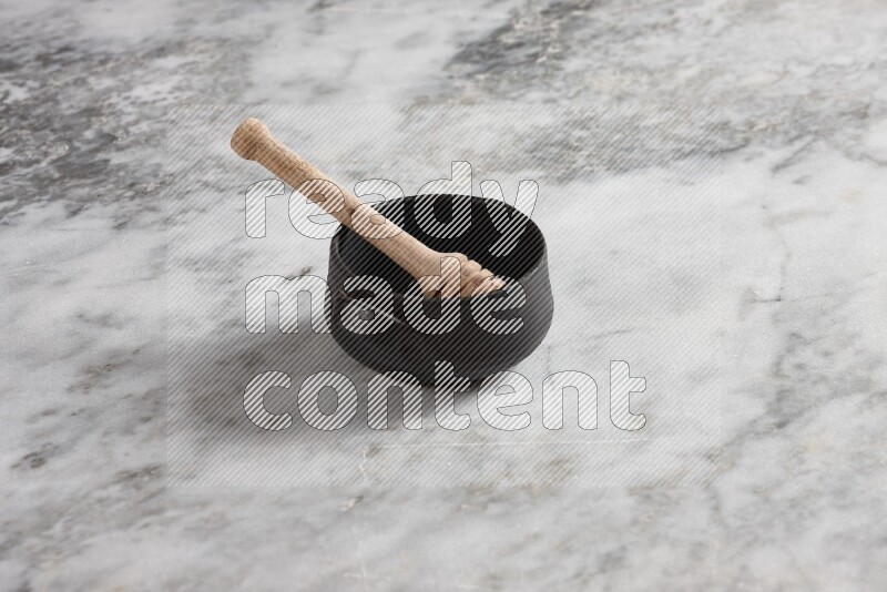Black pottery bowl with wooden honey dipper in it on grey marble background
