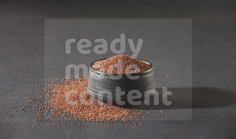 وعاء فخاري أسود ممتلئ ببذور حب الرشاد محاط بالبذور على أرضية سوداء