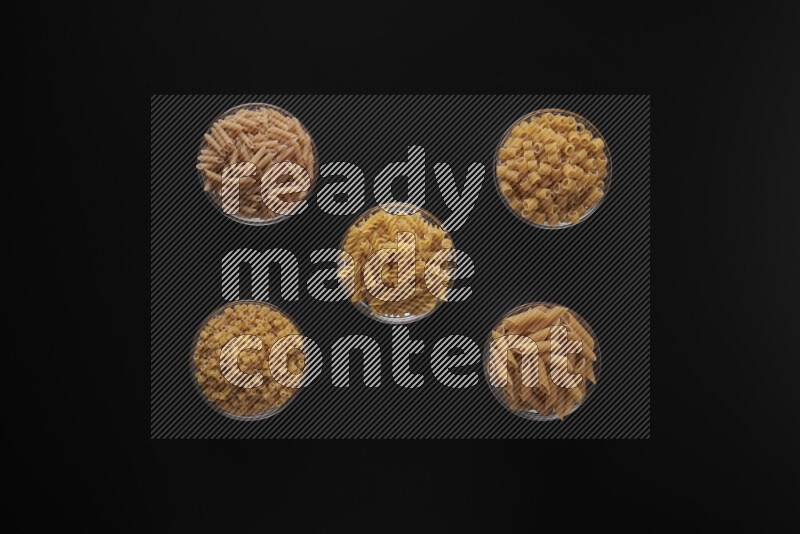 Different pasta types in 5 glass bowls on black background