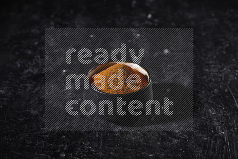 A black pottery bowl full of ground paprika powder on black background