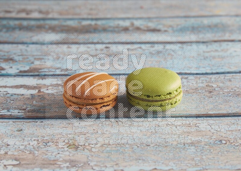 45º Shot of of two assorted Brown Irish Cream, and Green Pistachio macarons  on light blue background
