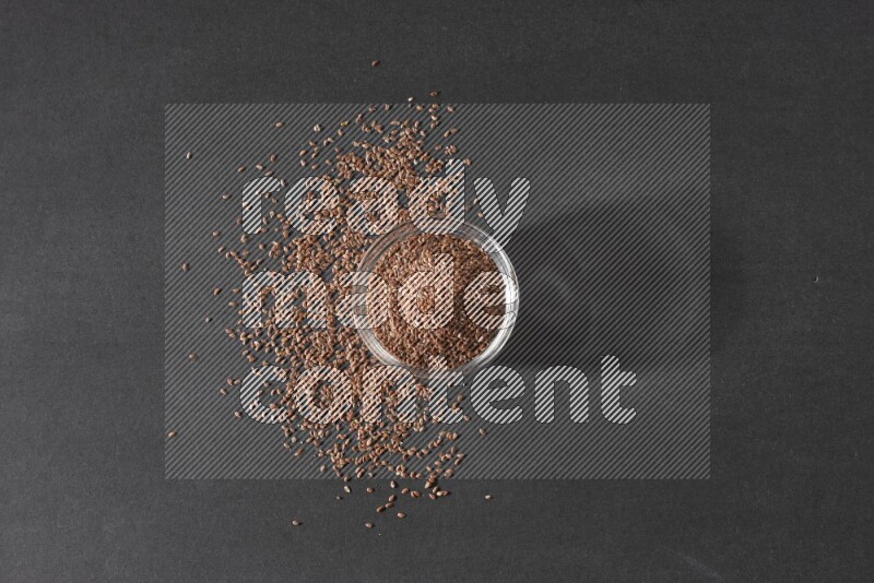 وعاء زجاجي ممتلئ بحبوب بذر الكتان محاط بالبذور على أرضية سوداء