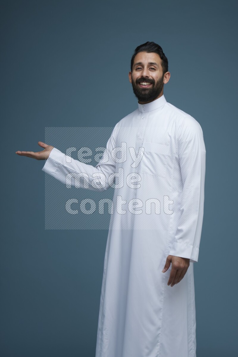 A man pointing in a blue background wearing Saudi Thob