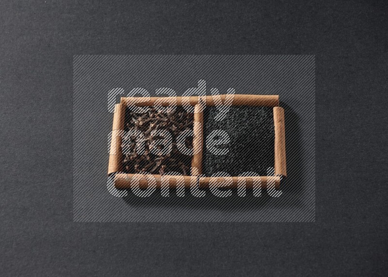 مربعان من أعواد القرفة ممتلئان بحبة البركة السوداء والقرنفل علي خلفية سوداء